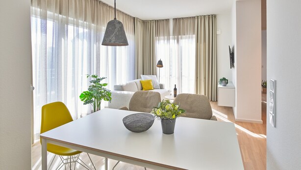 A modern dining area with a white table, yellow chairs, a black bowl, and a potted plant.