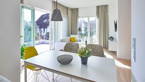 A modern hotel room with a dining area, a balcony with a view, and a living area with a sofa and chairs.