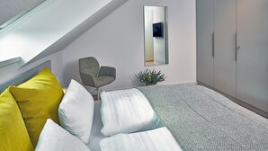 A modern bedroom with a bed, a chair, a plant, and a wardrobe.