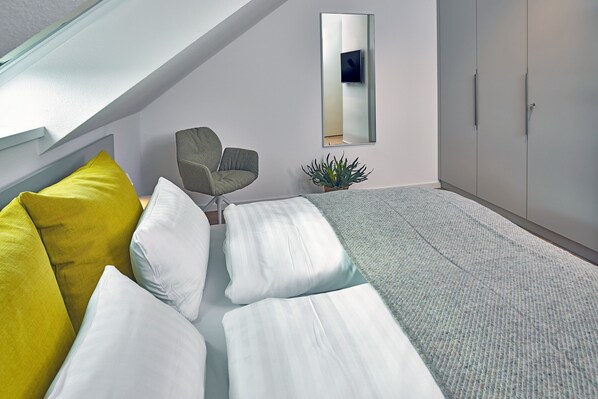 Un dormitorio moderno con una cama, una silla, una planta y un armario.