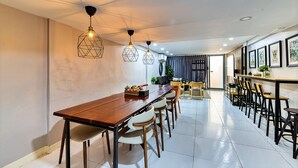 A modern dining area with a long wooden table, multiple chairs, pendant lights, and framed artwork on the walls.