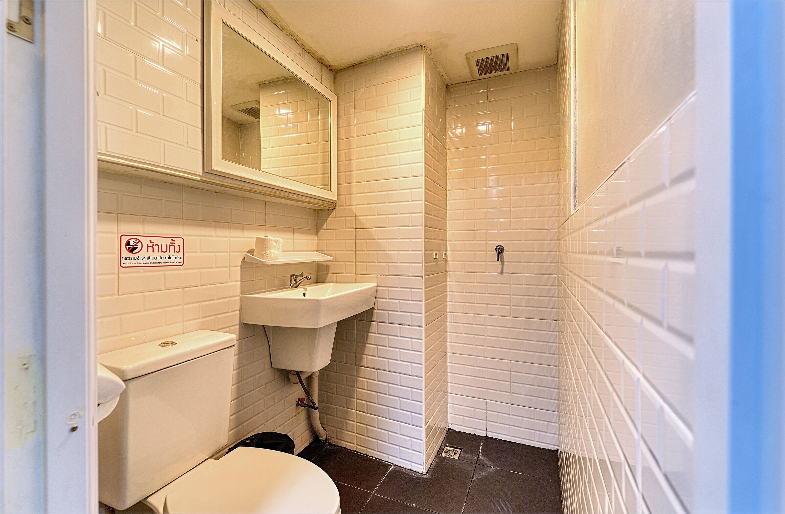 A small, clean bathroom with white tiles, a sink, a toilet, and a mirror.