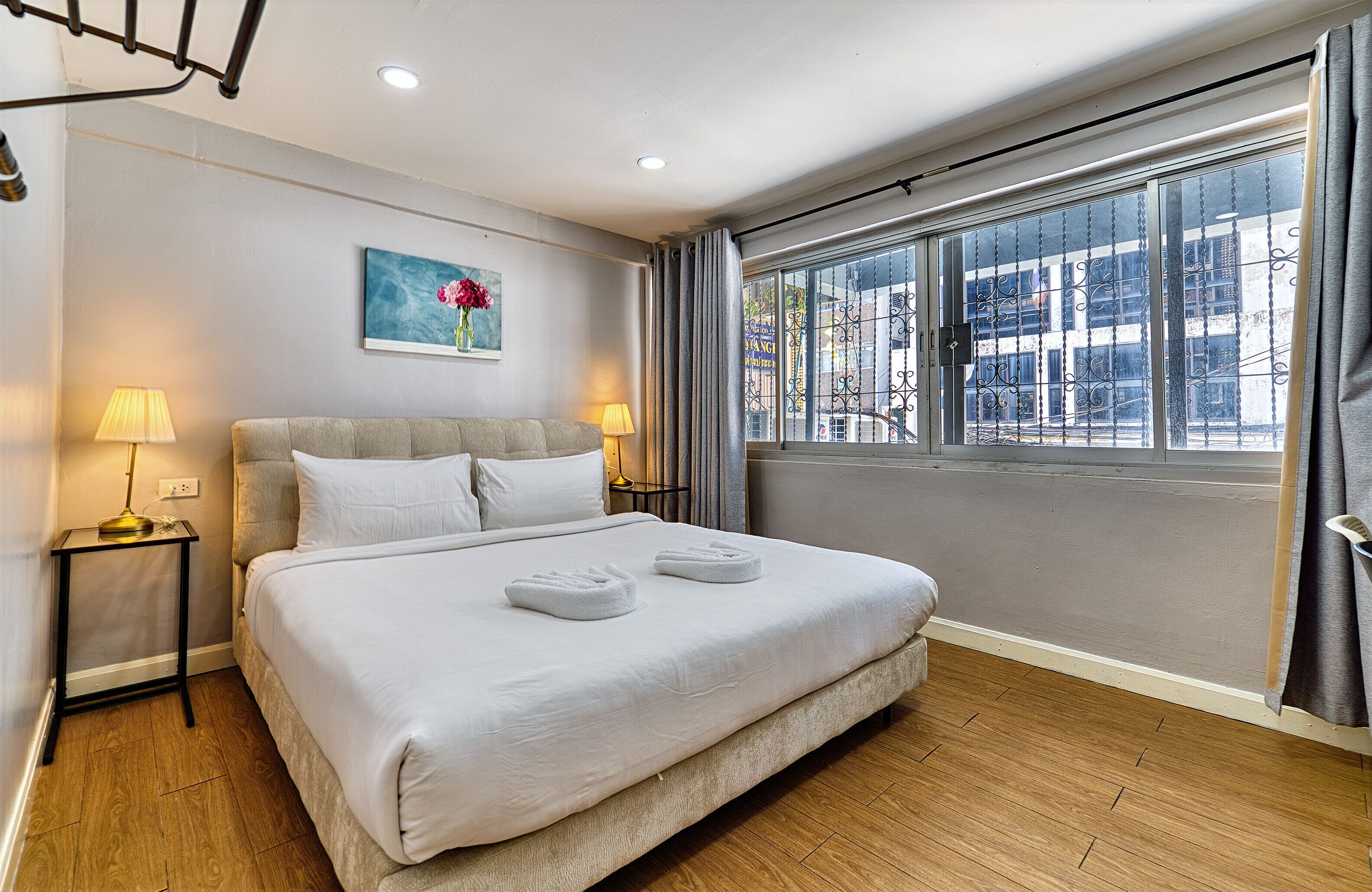 A hotel room with a large bed, two bedside tables with lamps, a painting on the wall, and a window with curtains.
