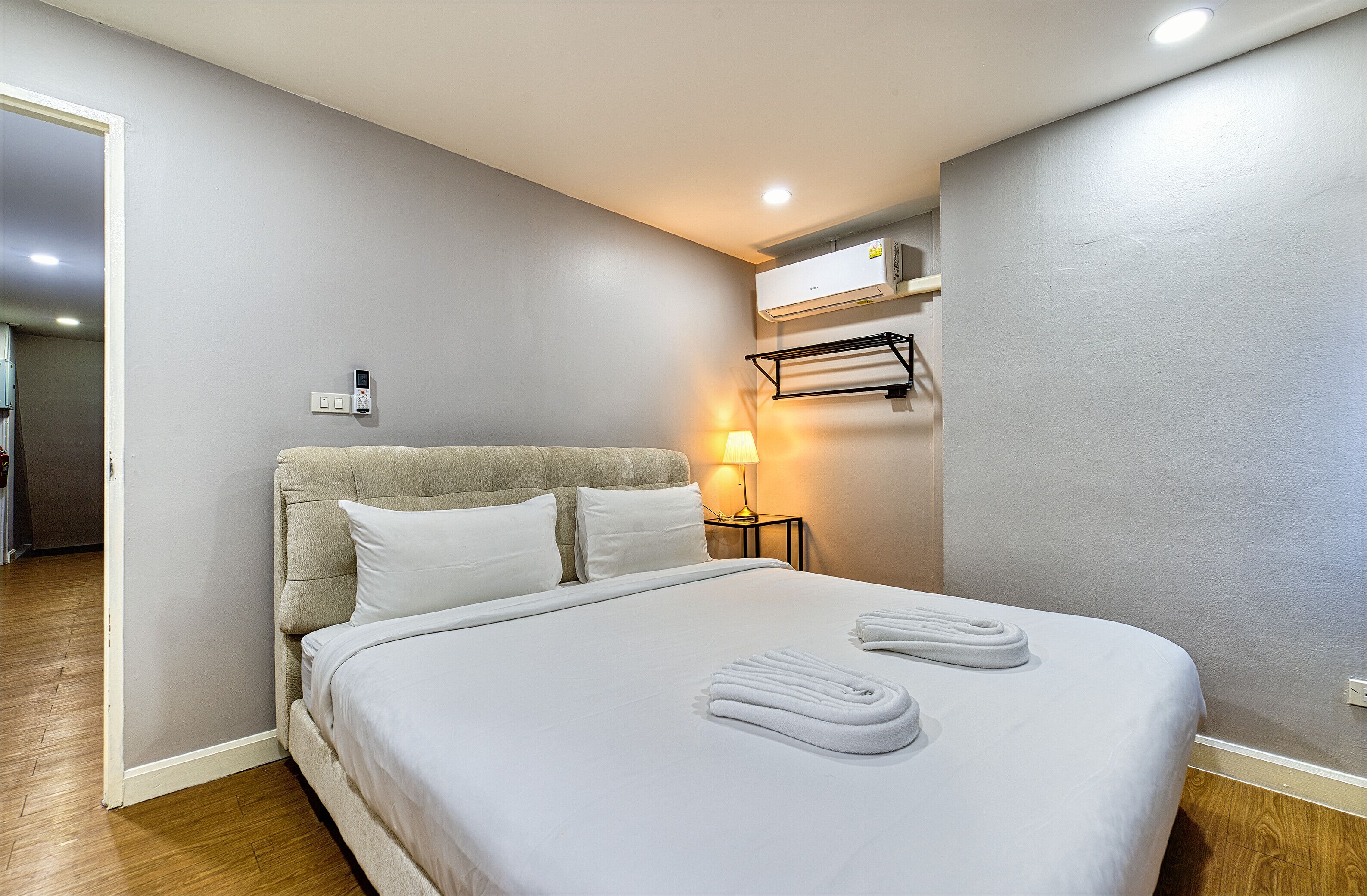 A neatly made bed with white linens and towels, a bedside lamp, and an air conditioning unit on the wall.