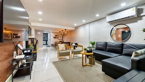 A modern living room with a black leather sofa, wooden chairs, a small table, and a round mirror on the wall.