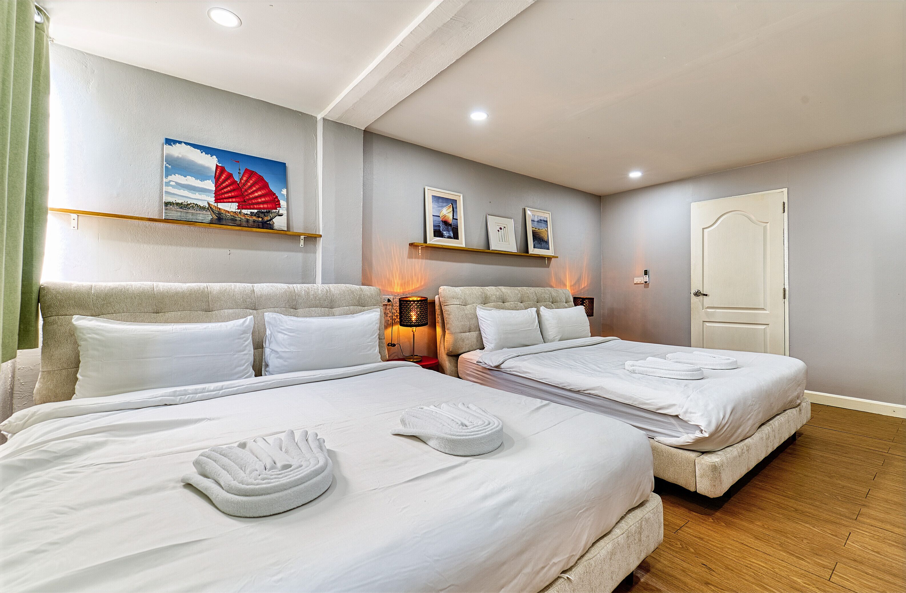 A hotel room with two beds, white linens, and towels. There are wall-mounted shelves with framed pictures and a door to the right.