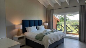 Een moderne slaapkamer met een groot bed, bedlampen, een nachtkastje en uitzicht op de omgeving vanaf een balkon.