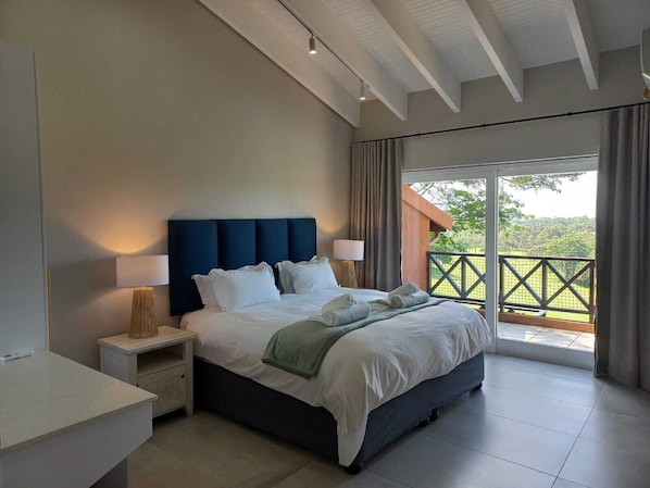A modern bedroom with a large bed, bedside lamps, a nightstand, and a view of the outdoors through a balcony.