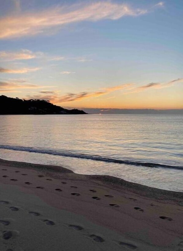 A beach with footprints leading into the water, a calm sea, and a sunset sky.