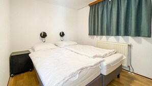A bedroom with a double bed, two wall-mounted lamps, a radiator, and a green curtain. - Stunning (sta)caravan in Putten (Putten)