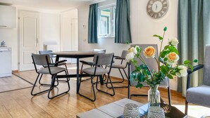 A modern living room with a round dining table, grey upholstered chairs, a vase with flowers, and a wall clock. - Stunning (sta)caravan in Putten (Putten)