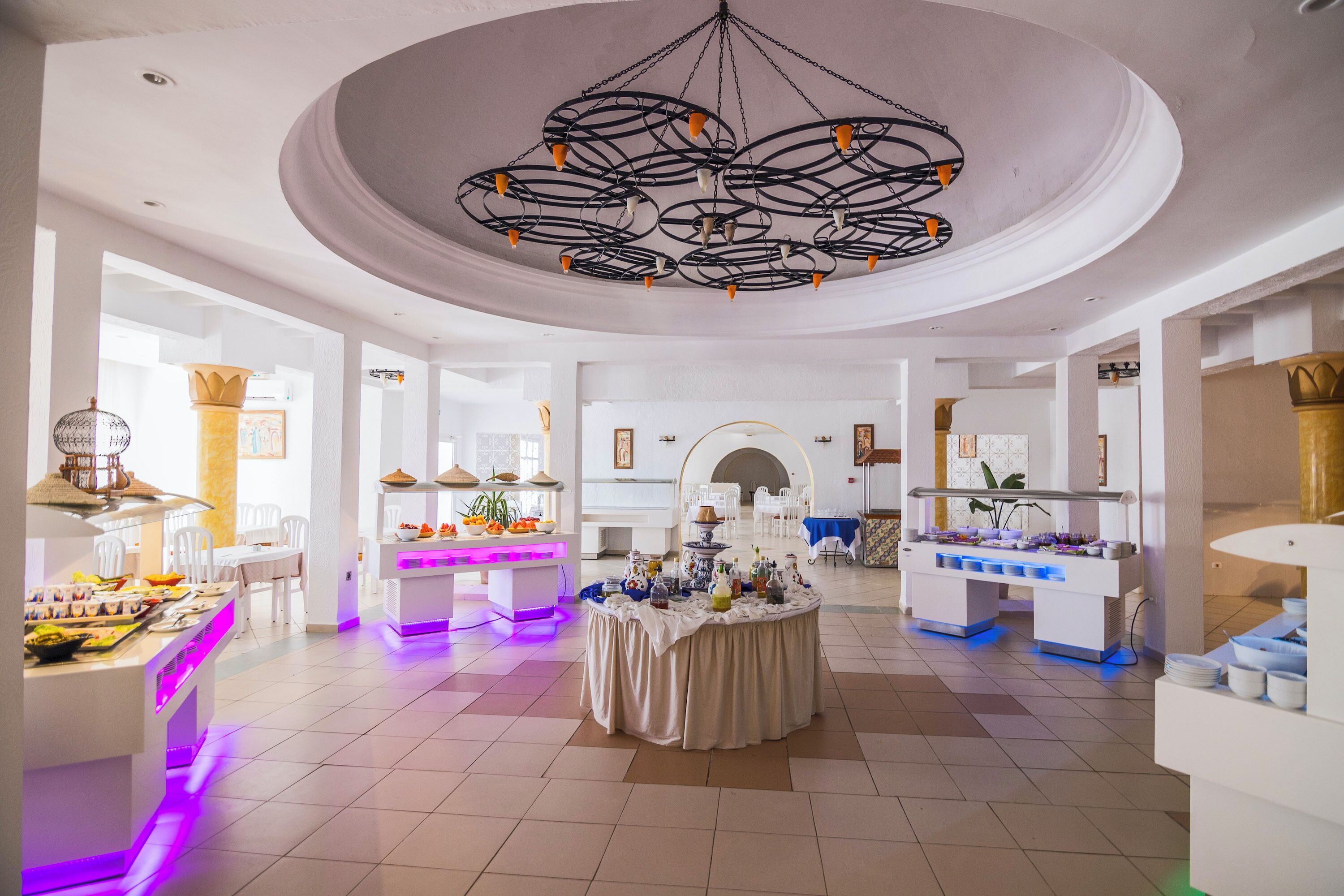 A spacious room with a central chandelier, white walls, and a buffet setup.