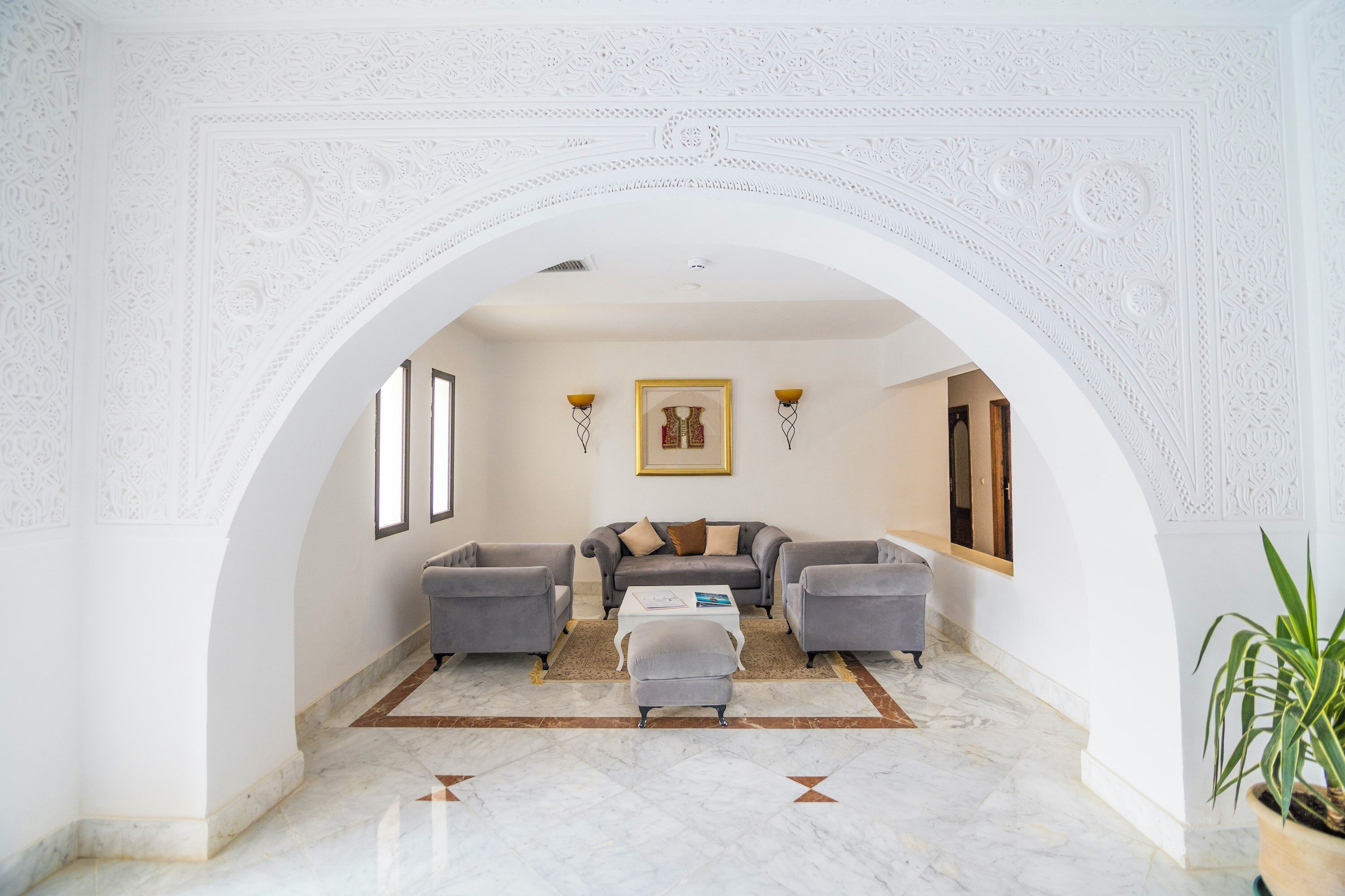 A spacious living room with a high arched doorway, a grey sofa set, a coffee table, and a framed picture on the wall.