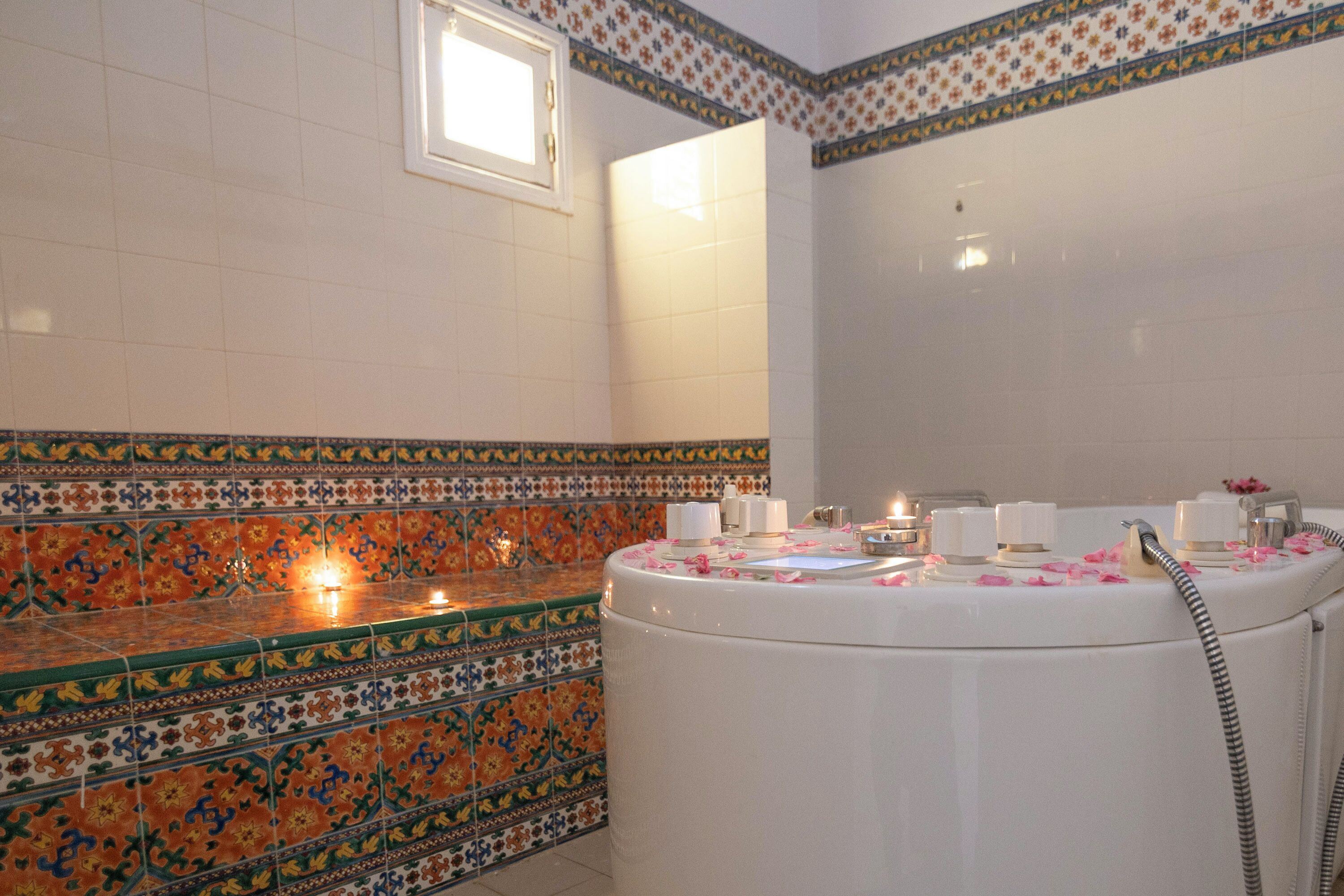 A bathroom with a white bathtub, a mirror, and a tiled wall with a floral pattern.