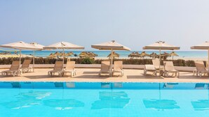Un espace aménagé au bord de la piscine, avec des chaises longues et des parasols, une vue dégagée sur la plage et une mer calme.