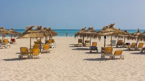 Une plage bordée de rangées de chaises longues et d’ombrelles en chaume.