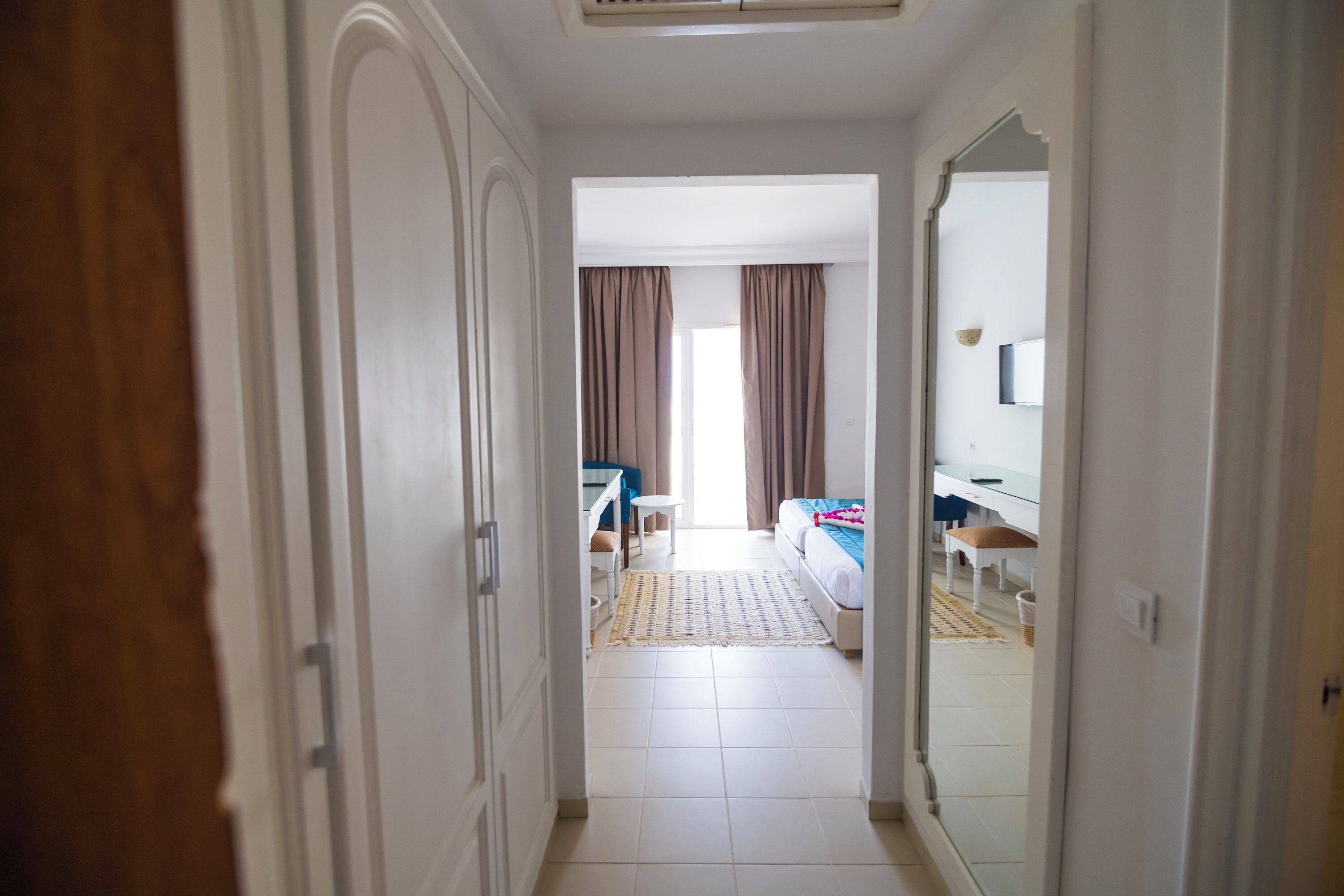 Pasillo de hotel que conduce a una habitación con cama, escritorio y silla.