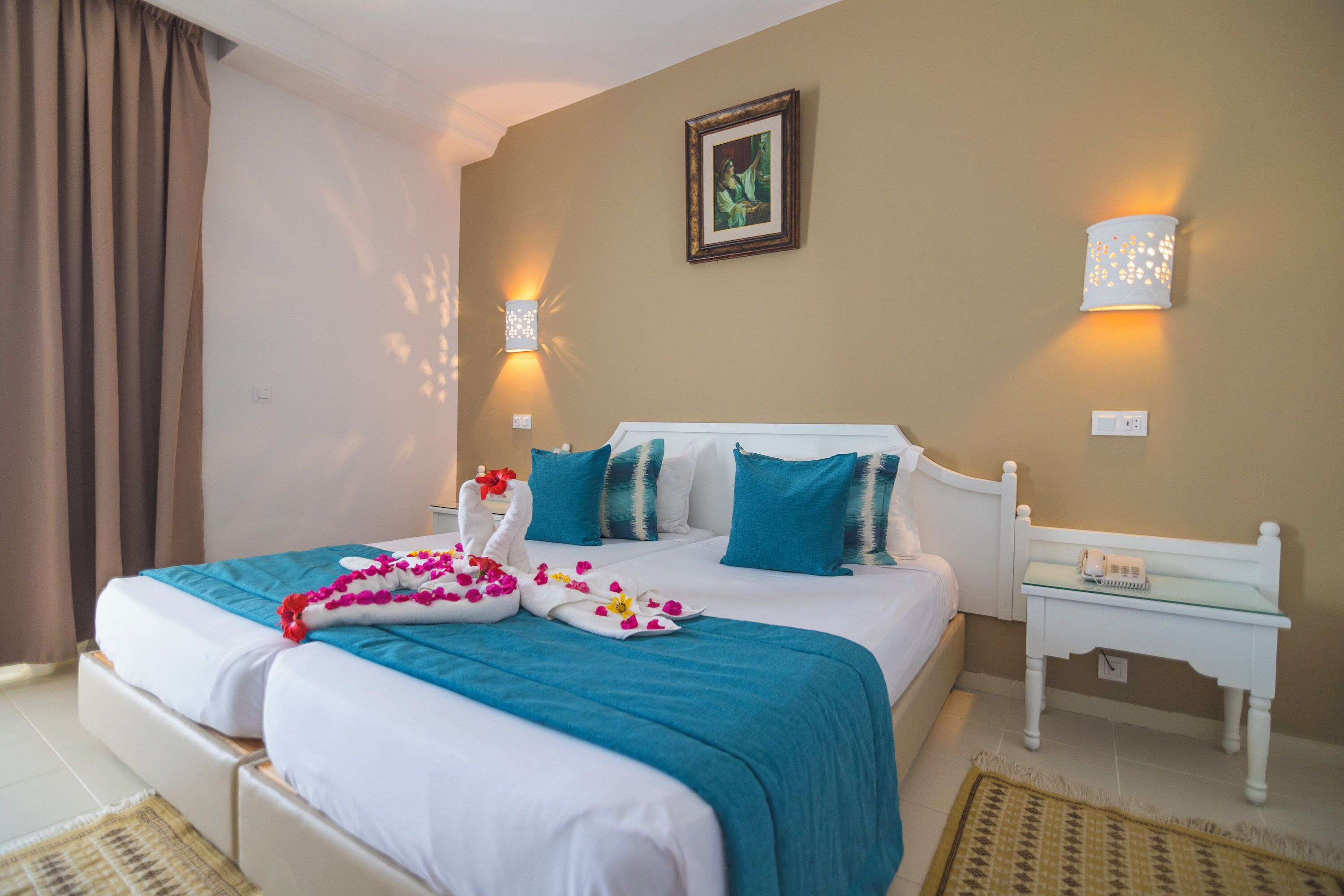 Une chambre d’hôtel avec un lit, une table de chevet, une lampe fixée au mur et un tableau encadré.