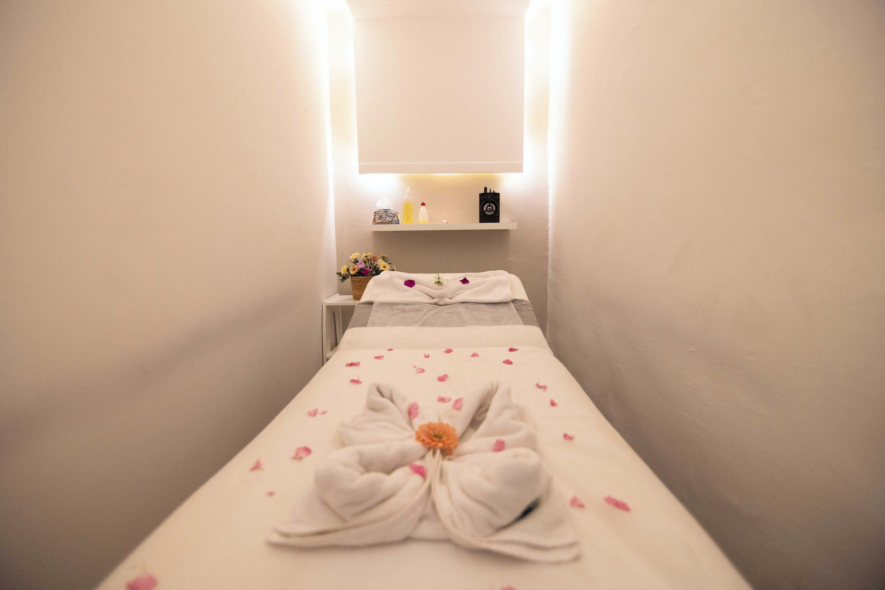A spa room with a massage table, a towel with a flower, and a shelf with toiletries.