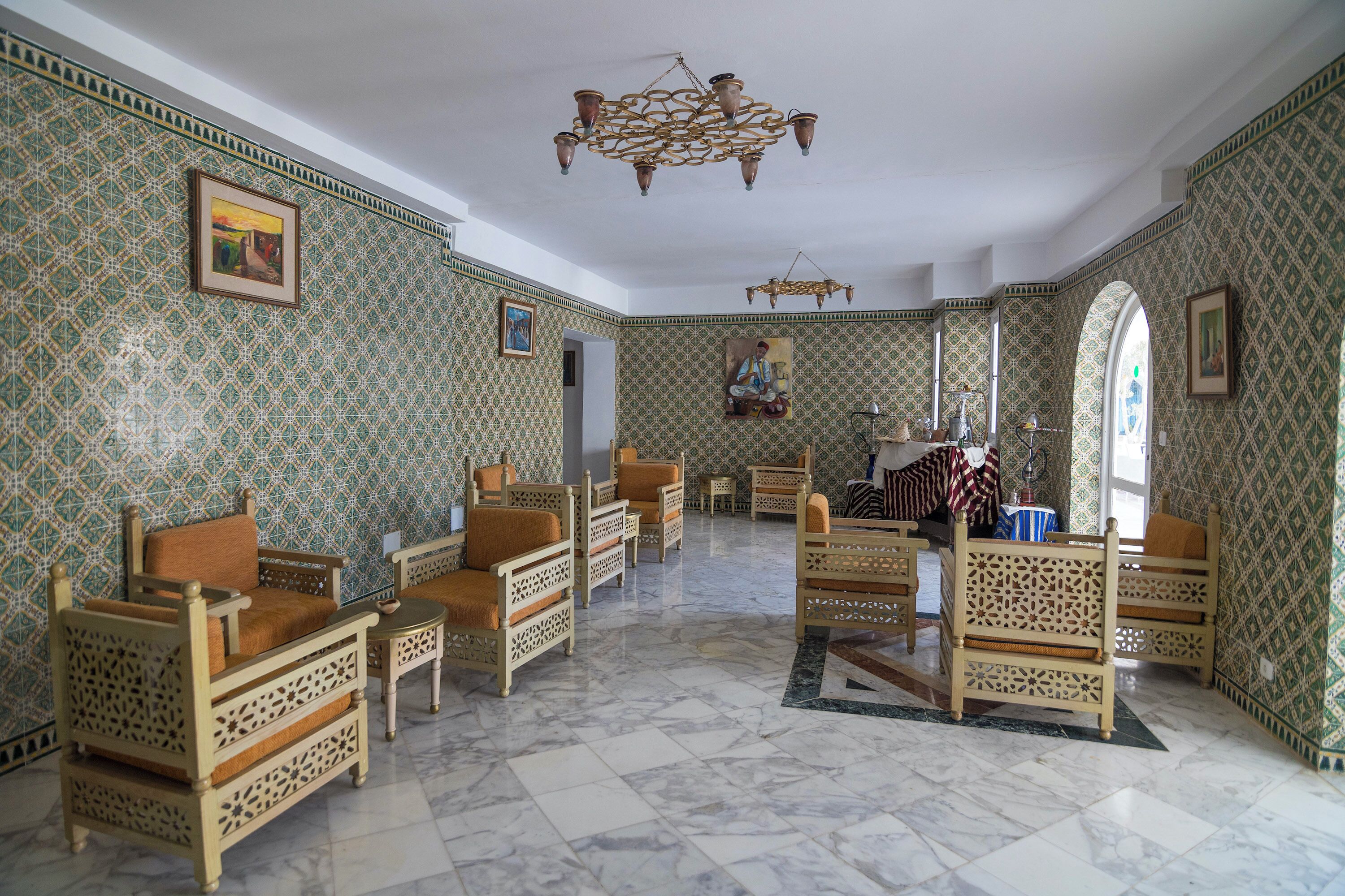 A room with patterned walls, a chandelier, and multiple seating areas with wooden furniture.
