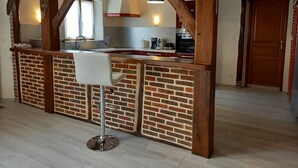 A kitchen with exposed wooden beams, a brick backsplash, and a bar area with a white stool. - Les Maisons du Théâtre Romain - 4 Gîtes - 10 Chambres (Le Vieil-Évreux)