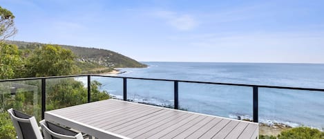 A wooden deck with a table and chairs overlooking a coastal view.