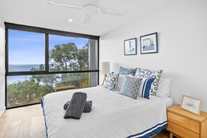 A bedroom with a large window, a bed with patterned pillows, a bedside table with a framed picture, and a ceiling fan. - Wonder Wye (Wye River)