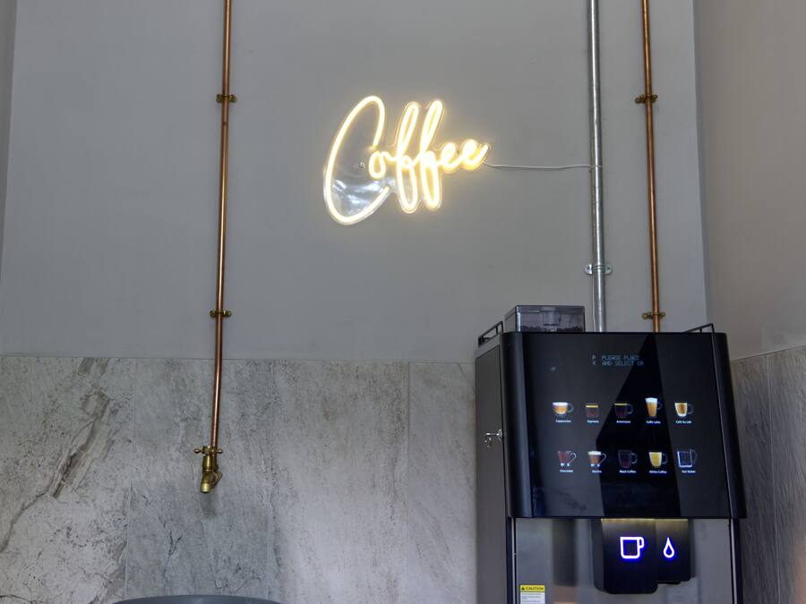 A coffee station with a neon sign, a coffee machine, and a cup on a marble countertop.