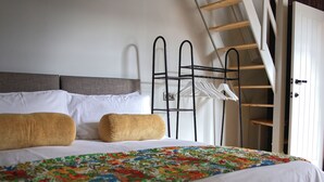 Una cama bien hecha con una colcha estampada, dos almohadas y un tendedero de metal con perchas blancas.