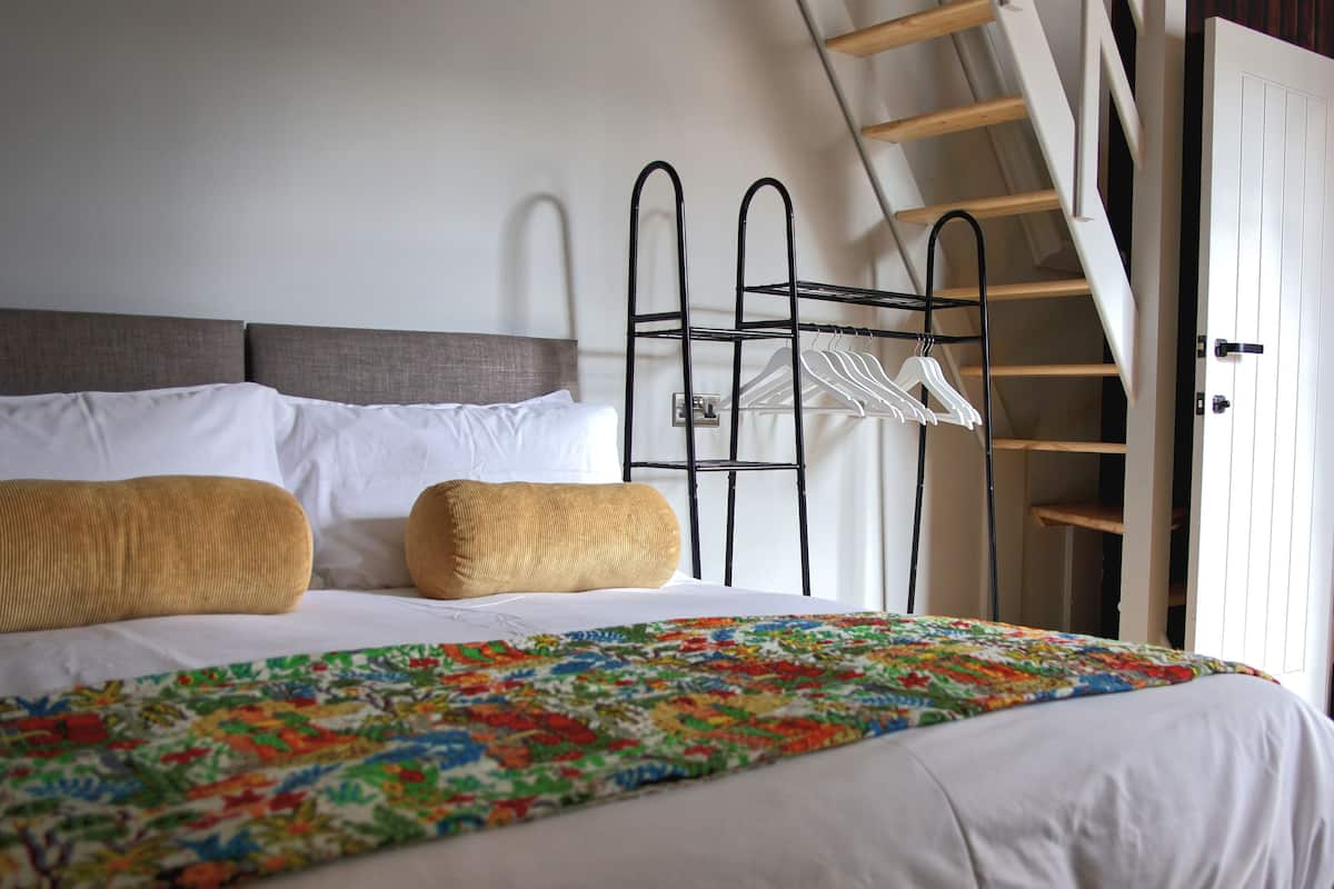 A neatly made bed with a floral bedspread, two pillows, and a metal drying rack with white hangers.