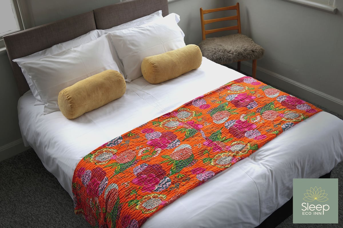 A neatly made bed with white linens, two mustard-colored pillows, and a colorful floral blanket.