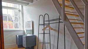 Una habitación con ventana, un escritorio y un perchero con ropa colgada.
