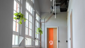 Un pasillo espacioso con ventanas amplias, suelo de madera y una puerta con diseño geométrico.