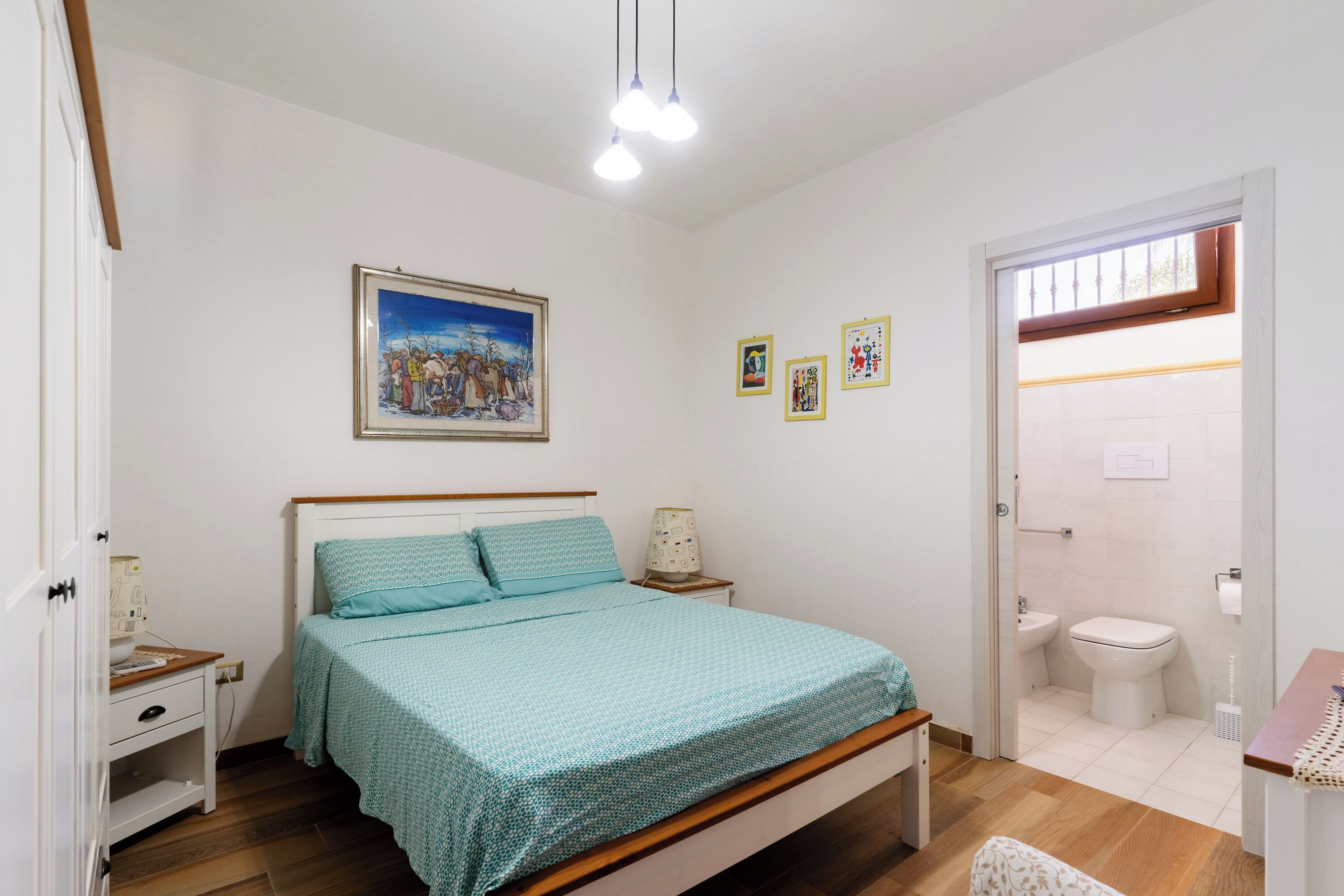 Una camera da letto con un letto, un comodino e una scrivania. C'è un bagno con il water, un lavandino e uno specchio.