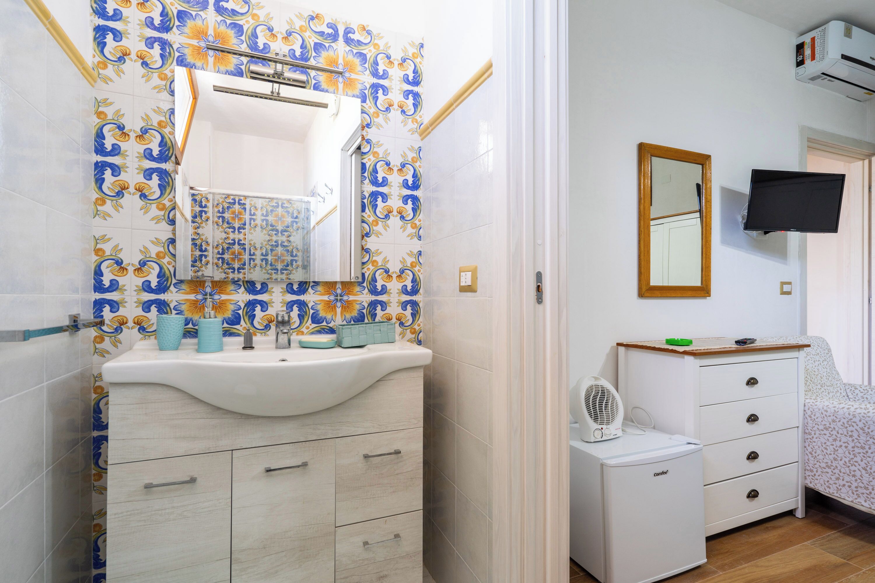 Un bagno con un lavandino bianco, uno specchio e una parete piastrellata con motivo floreale.