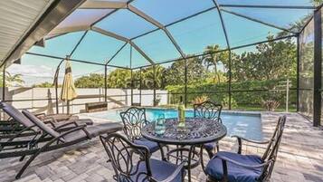Um pátio externo com piscina, espreguiçadeiras e uma mesa com cadeiras.