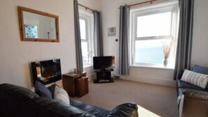 A living room with a black leather sofa, a television, and a window with curtains. - 2 Marine Parade , 2, ventnor, GB (ventnor)