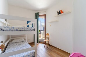 Quarto com beliches, uma cadeira de madeira, uma estante com livros e uma porta que dá para área externa.