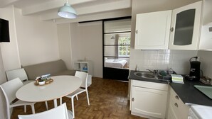 Une cuisine compacte avec des meubles blancs, un évier et une cuisinière. On y trouve également un coin repas avec une table ronde et des chaises blanches.