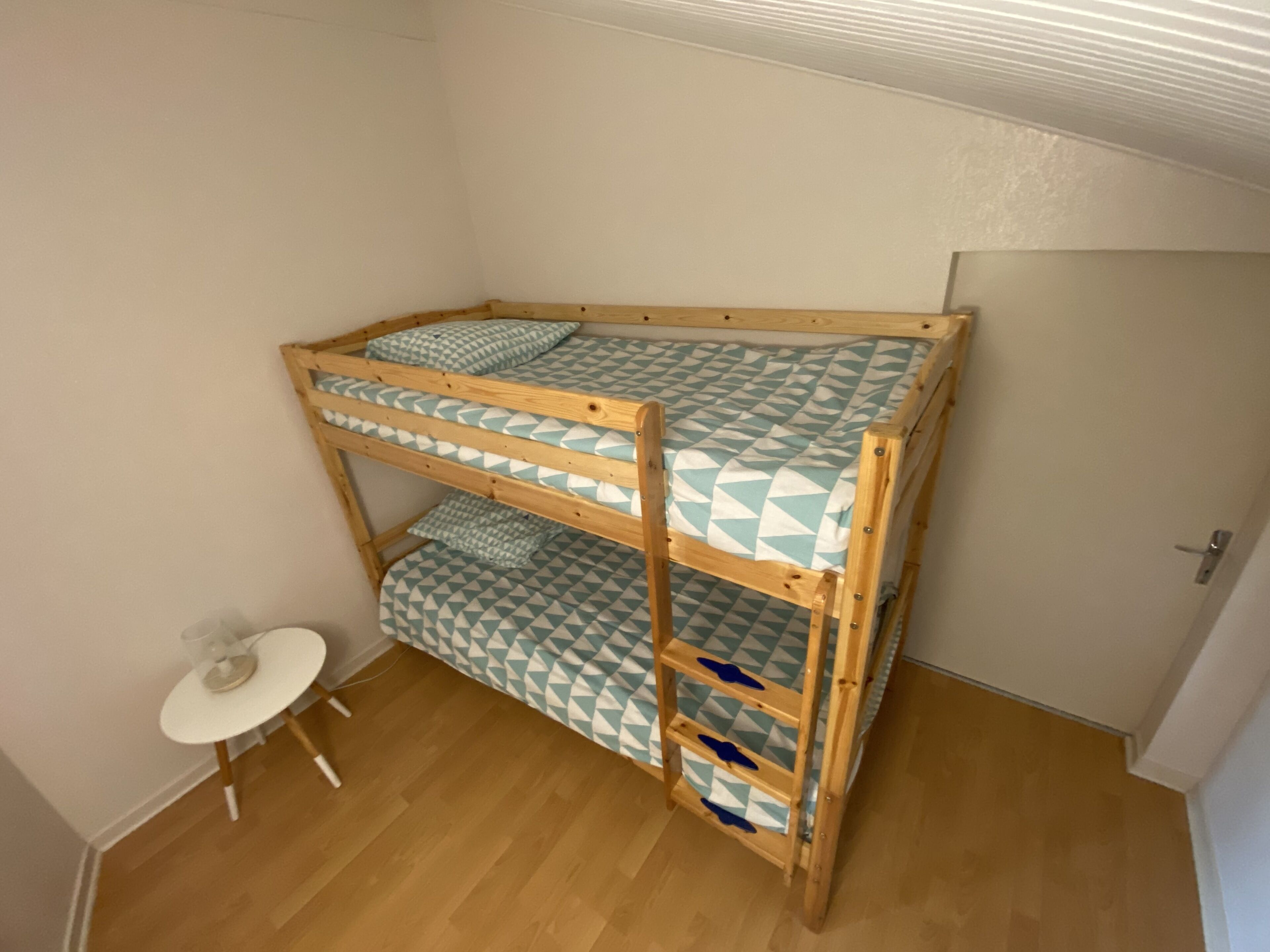 Una cama litera con ropa de cama estampada en una habitación con piso de madera y una pequeña mesa.