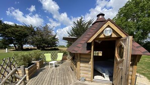 Une cabane en bois avec un toit en pente, une petite véranda avec deux chaises et un lit à l’intérieur.
