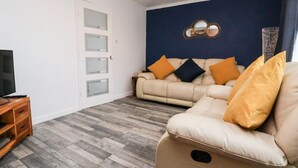 A living room with a beige sofa, a television on a wooden stand, and a dark blue accent wall. - 17 Third Avenue (Prestatyn)