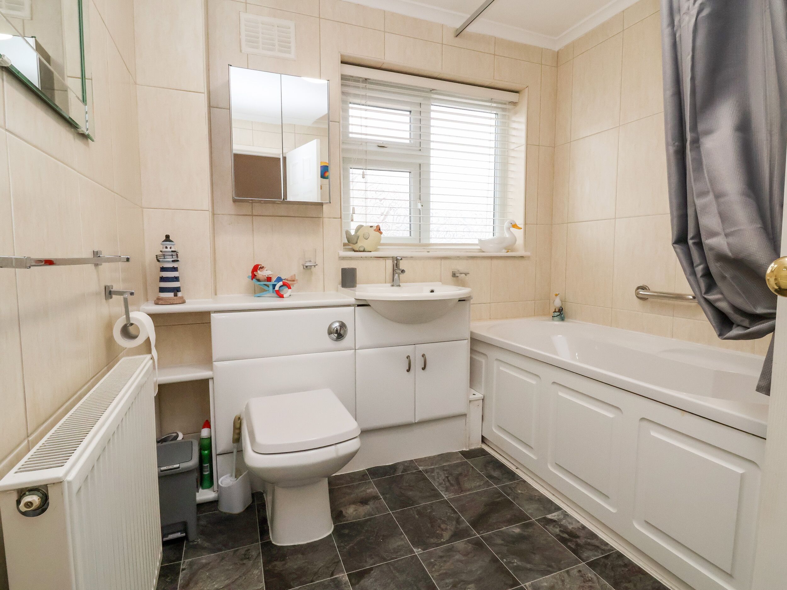 A bathroom with a toilet, sink, and bathtub. There is a mirror above the sink and a window with blinds.