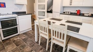 A modern kitchen with white cabinetry, a black countertop, and a dining area with white chairs. - 17 Third Avenue (Prestatyn)