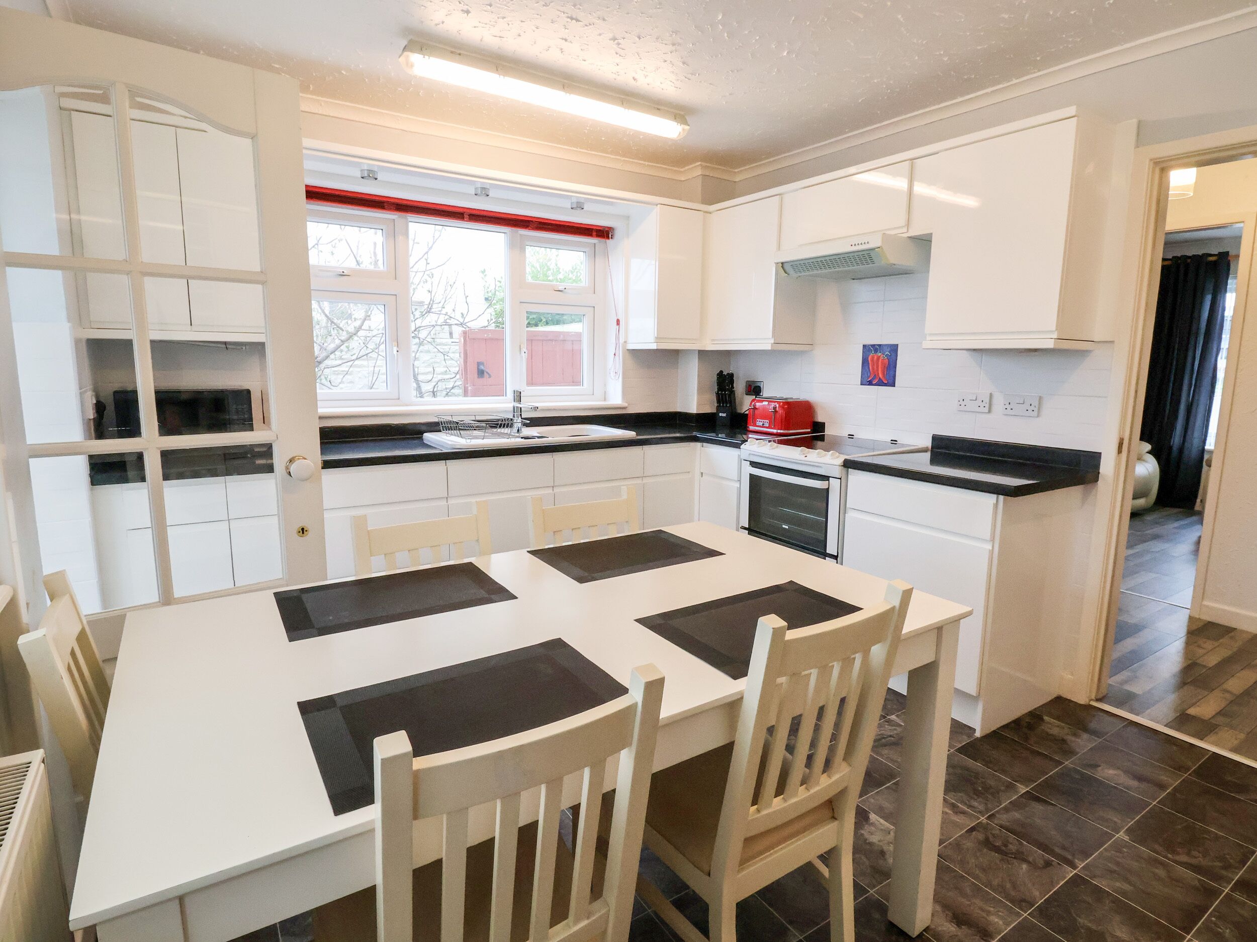 Een moderne keuken met witte kasten, een zwart aanrecht en een eethoek met een witte tafel en stoelen.