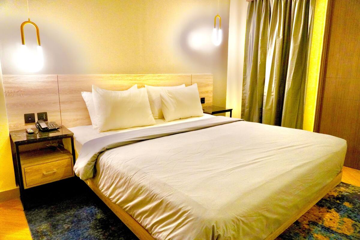 A hotel room with a large bed, two bedside tables, a nightstand, a telephone, and a wall-mounted light fixture.