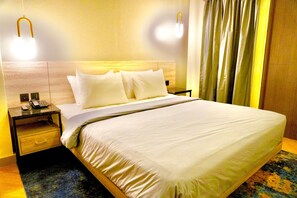 A hotel room with a large bed, two bedside tables, a nightstand, a telephone, and a wall-mounted light fixture. - Series Hotel Sudirman (Jakarta)