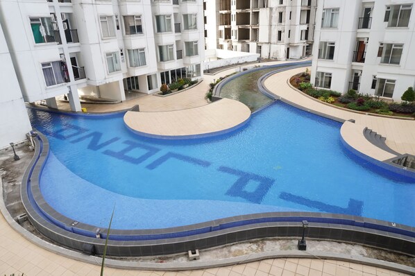 A swimming pool with a curved design, surrounded by a tiled walkway and a landscaped area with plants. - Series Hotel Sudirman (Jakarta)