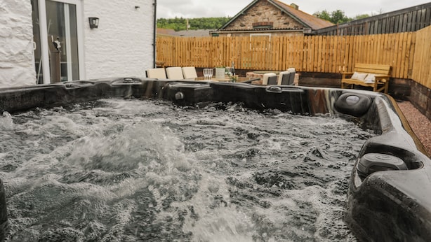 A hot tub area with stone seating and a wooden fence in the background. - Plas Coch (Saint Asaph)
