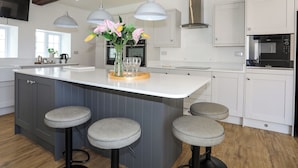 A modern kitchen with a large island, pendant lights, and bar stools. - Plas Coch (Saint Asaph)
